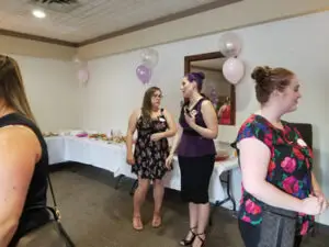 People mingling at a baby shower in the fireplace room.